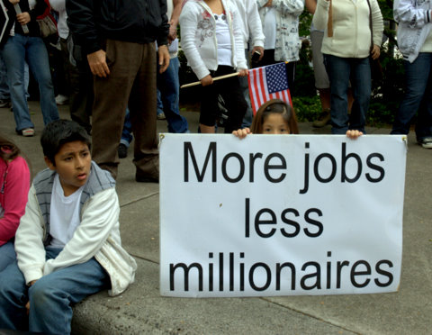 More jobs less millionaires A small child at a protest march holding a poster reading 'More jobs less millionaires'.